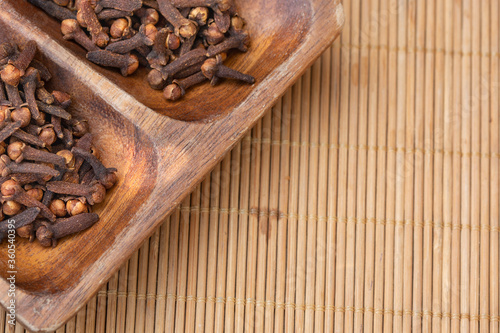dried cloves in a wooden dish and clear cloves on a wooden background.