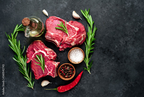 Two raw beef steaks with spices on a stone background with copy space for your text