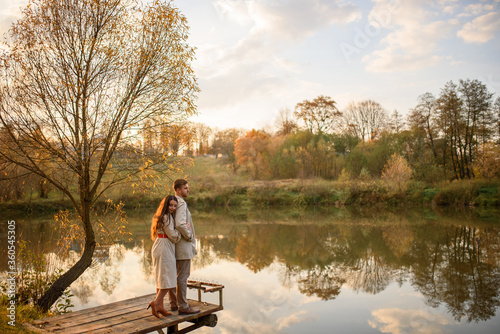 A romantic young couple stands on a pier near the lake. Fall.