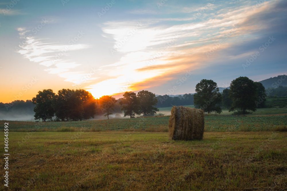 Hay bales rolled on field at sunrise with fog creates amazing sky in early summer Sussex County NJ 