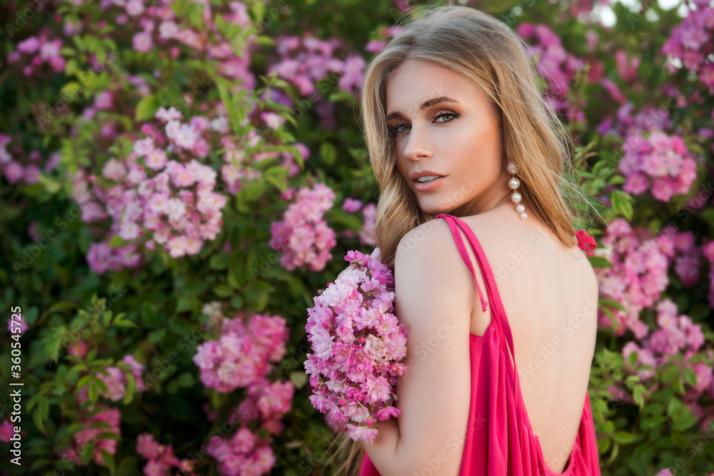 Beautiful woman in pink dress and blond long hair collect pink roses. Beauty and fashion