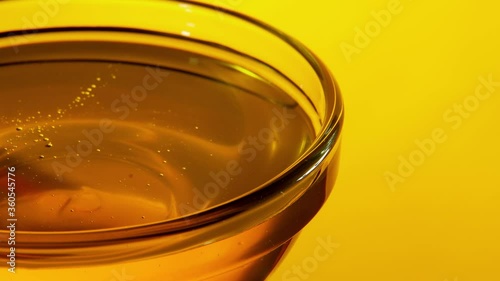 Close-up side motion of a small glass bowl of honey on a yellow background with backlight. 