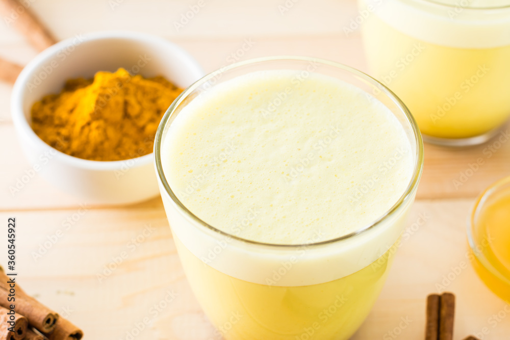 Detox drink. Golden milk with turmeric and cinnamon in a transparent glass on a wooden table. Close-up Detox drink. Golden milk with turmeric and cinnamon in a transparent glass on a wooden table. Close-up
