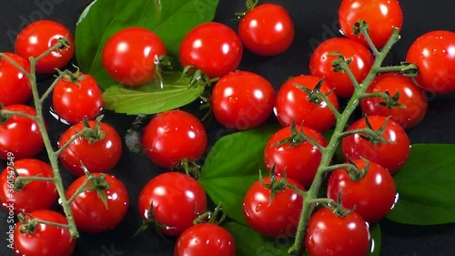 Top view of red cherry tomatoes in water on a dark background under water drops in slow motion