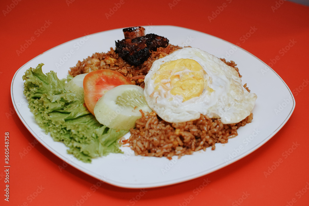 Indonesian fried rice with sunny side up and grilled spare ribs. fresh tomato lettuce and cucumber Indonesian fried rice with sunny side up and grilled spare ribs. fresh tomato lettuce and cucumber