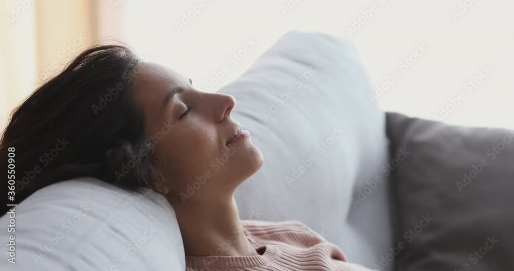 Side close up head shot view serene young attractive woman daydreaming on comfortable sofa alone. Happy lady enjoying peace of mind, sleeping napping breathing fresh air lounge on couch at home. Side close up head shot view serene young attractive woman daydreaming on comfortable sofa alone. Happy lady enjoying peace of mind, sleeping napping breathing fresh air lounge on couch at home.