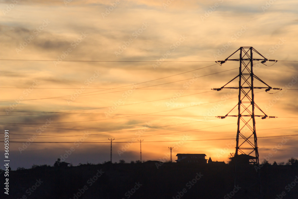 Electricity pylon and village silhouette at sunset landscape. Energy concept.