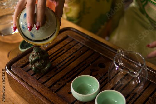 A girl in a Japanese kimono is holding a bowl with Chinese Lujing tea. Table with bowls, a wooden tray, a transparent cup. Good for restaurants, tea establishments, banners, posters, flyers. 