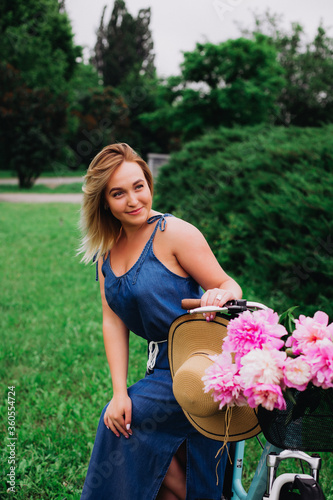 A girl in a blue dress on a vintage bike on a summer morning in greens with pink peonies. Beauty. Model. Summer. Retro.
