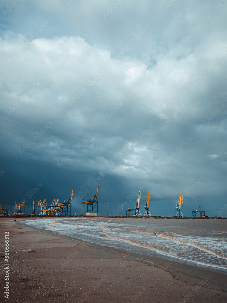 Port cranes under the dark clouds after the thunderstorm. Dramatic stormy sky. Industrial landscape. Idle cranes in front of storm clouds