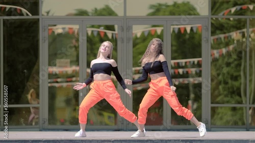 two young women with long hair in tracksuit dancing dancehall twerk, street modern dance in front of the building. Booty Dance