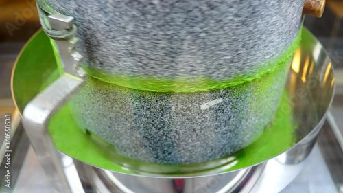 Matcha green tea grinding stone machine in motion with vibrant colorful powder closeup in factory or tea shop