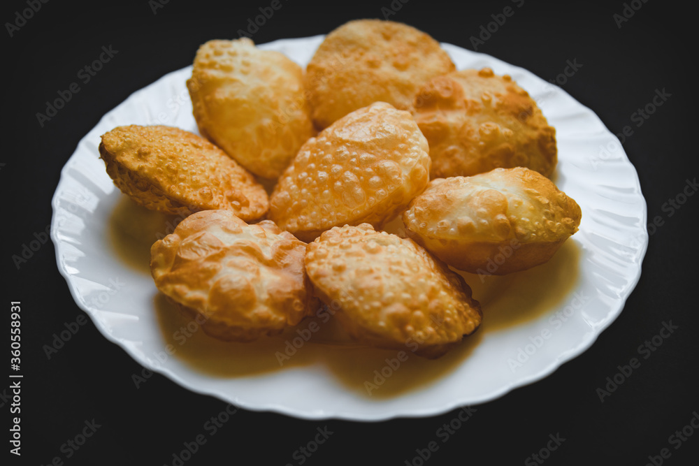 Traditional Indian deep fried poori on white plate with black background.