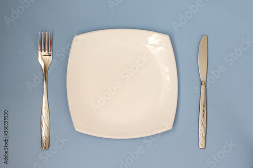 Empty plate, fork and knife over blue background. Clean plate and cutlery on light background. Top view.
