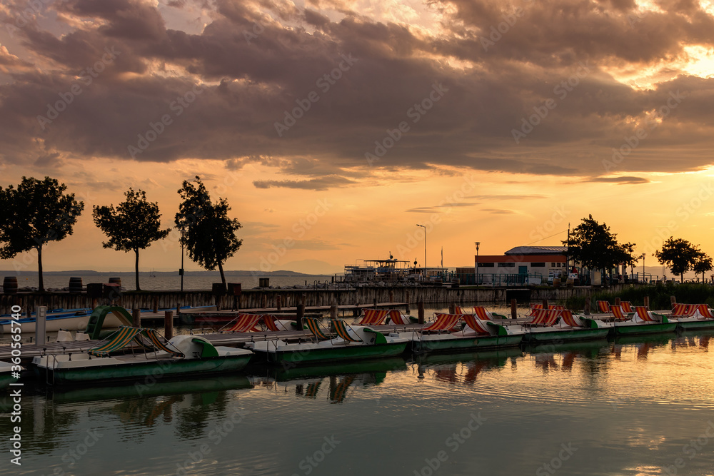 Wooden pier with a boat in the town of Podersdorf on Lake Neusiedl in Austria. In the background is a dramatic sunset sky.