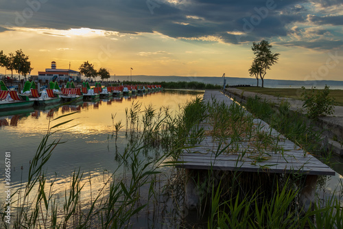 Wooden pier with a boat in the town of Podersdorf on Lake Neusiedl in Austria. In the background is a dramatic sunset sky. photo