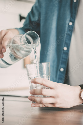 The man pours himself a glass of clean water. A carafe of water on the kitchen wooden table. Bottle of water. the concept of a healthy lifestyle