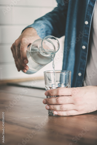 The man pours himself a glass of clean water. A carafe of water on the kitchen wooden table. Bottle of water. the concept of a healthy lifestyle