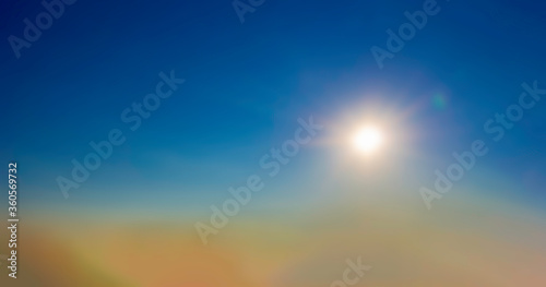 soft image of sun setting with amber clouds below and clear blue sky above as rays of light come from sun