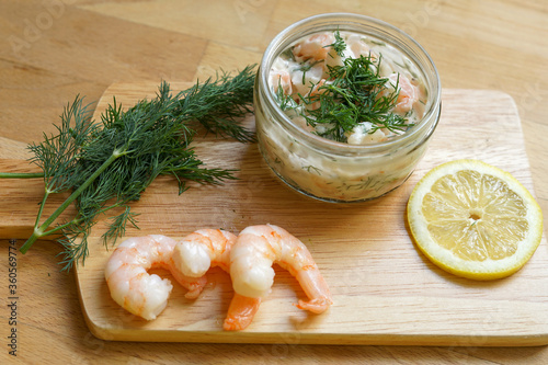 Scandinavian Food - Wooden chopping board with fresh shrimps, dill, slice of lemon and glass jar of traditional Skagen 
