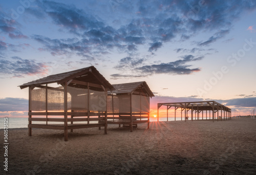 Deserted sandy beach with wooden bungalows at the sunset. Quiet evening on the seashore. Beautiful sky with setting sun, silence, romance, solitude. Copy space on the sky. © vitaliiaberestok
