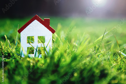 Fotografía small white toy house on green grass in sunshine with copy space for real estate
