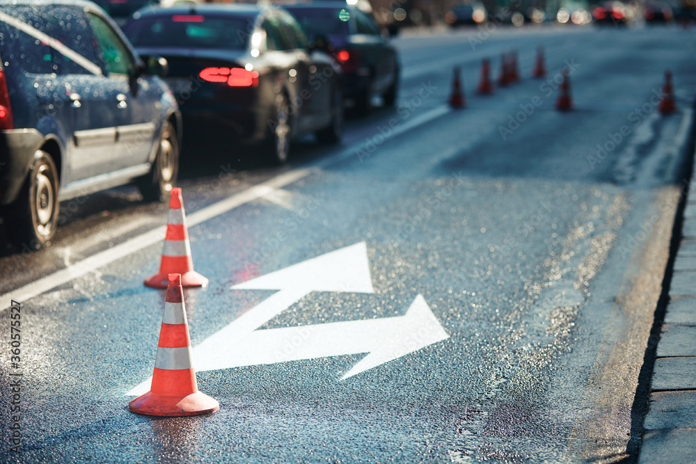 Orange safety traffic cones on the closed lane on the road, road marking. Direction of detour, roadworks. Road signs denoting road repairs Orange safety traffic cones on the closed lane on the road, road marking. Direction of detour, roadworks. Road signs denoting road repairs