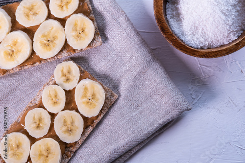 Multi seed crispbread with banana's slices, peanut butter and coconut on white background. Swedish and healthy snack. Top view.