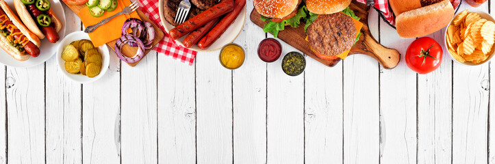 Summer BBQ food table scene with hot dog and hamburger buffet. Above view top border over a white wood banner background. Copy space.