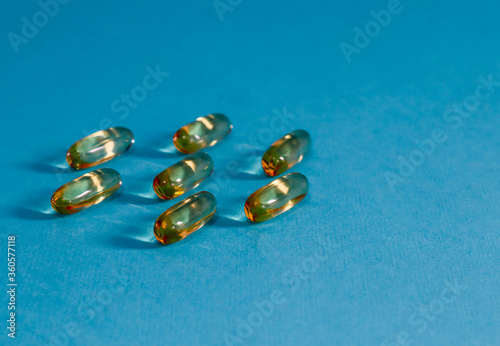 Transparent orange pills on blue paper background  closeup side view.