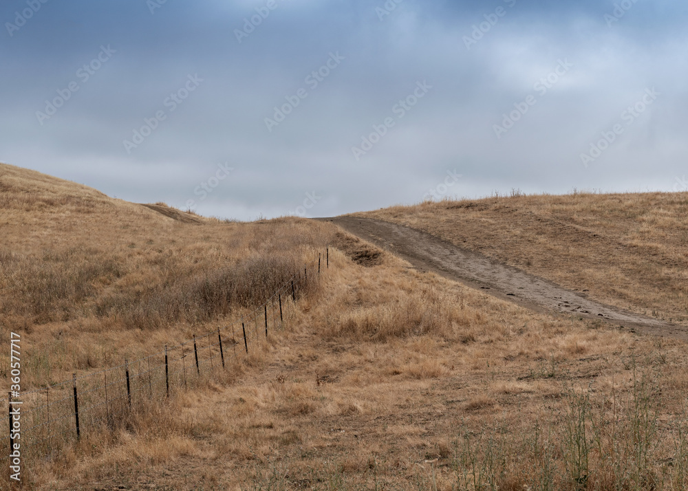 Briones Regional Park hiking trail on a partly cloudy day, featuring brown grass and a fence, Martinez, California, USA