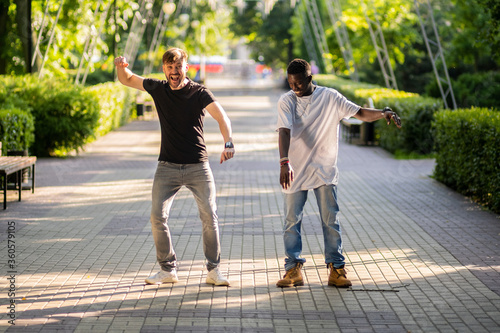 Black and white guy have fun and dance on the street in the Park. Interracial friendship