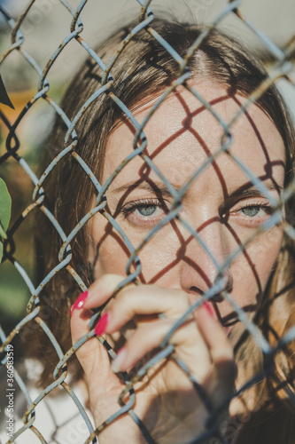 Close-up. The face of a young girl behind a metal fence