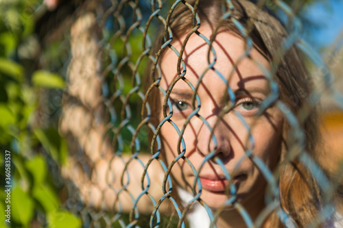The girl in the park looks through a metal fence.