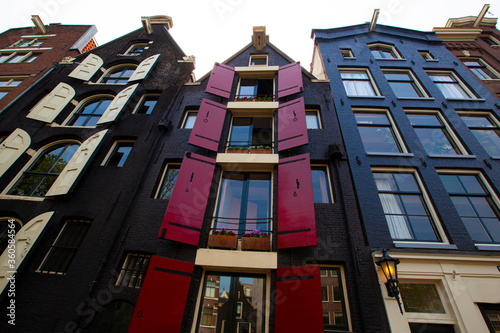 Canvas Print Close up image of Amsterdam's traditional narrow and tall houses with vibrant colored brick facades which harbor decorative elements including flower pots and colorful wooden window shutters