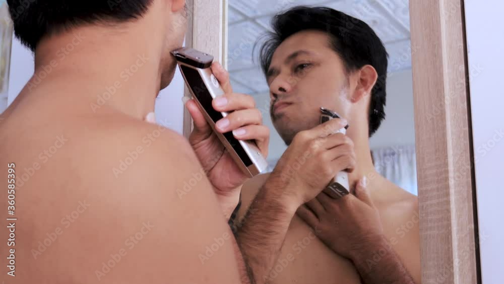 Young Asian man shaves with an electric shaver, Concept Stay home Young Asian man shaves with an electric shaver, Concept Stay home