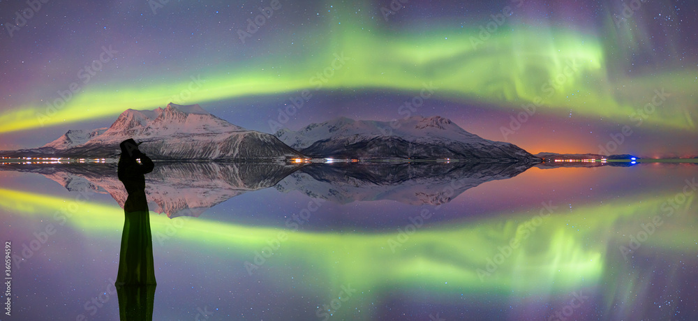 Young girl in dress and black hat walking on the water -  Northern lights (Aurora Borealis) in the sky over Tromso,  Norway