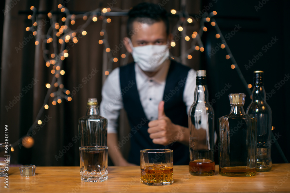 Barman pouring whiskey wearing  protective mask on the bar counter 