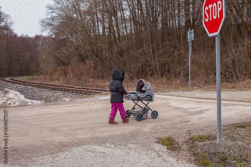 Little child with childish buggy close to railway crossing. Dangerous situation theme. Little infant near trackage. photo