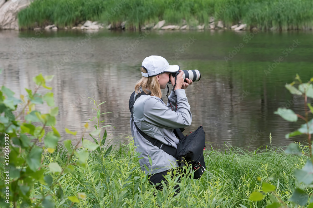 Outdoor photo trip. A girl with a photo camera on the bank of the river.