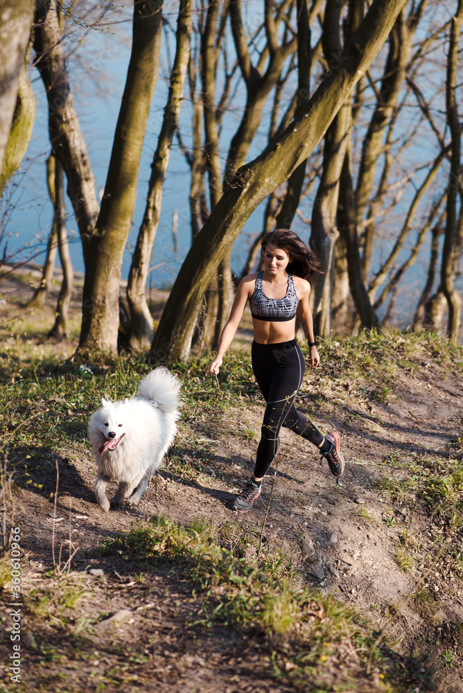 Athletic woman running with white fluffy dog outdoors Athletic woman running with white fluffy dog outdoors