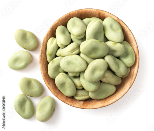 uncooked dried green broad beans in the wooden bowl, isolated on white background, top view