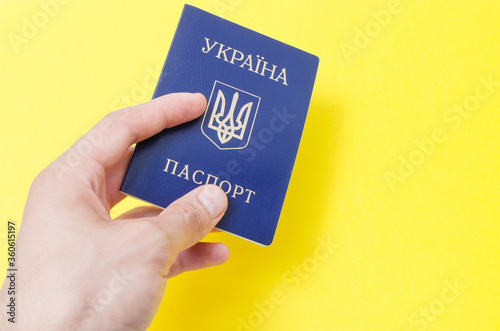 Ukrainian passport on a yellow background. Man's hand holds a Ukrainian passport in hand, gives the passport . The passport of the citizen of Ukraine in the macro. Passport General plan and close-up