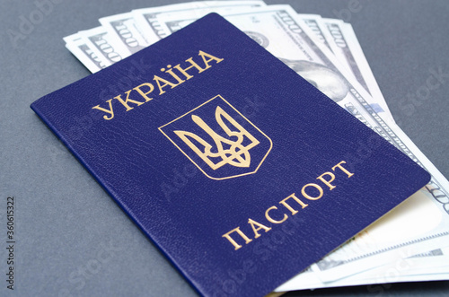 Ukrainian passport on a black background. $ 100 dollars are inside the passport at different angles