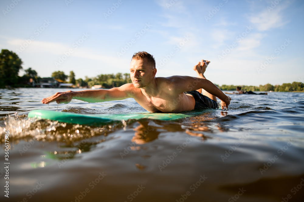 man lies on a surfboard, rows his hands and floats on the river.