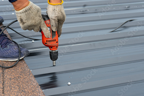 Workers installing the metal sheet roof by electrical drilling machine. Selective focus on the drilling tool while building the roof
