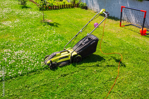 Lawn mower cutting green grass in backyard photo