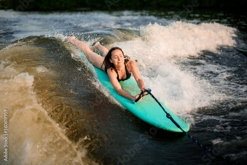 Young active woman lying on the wakesurf holding rope of motorboat