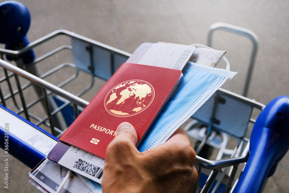 Fényképezés Traveller holding passport, face mask, boarding pass and map, hand on luggage trolley in airport