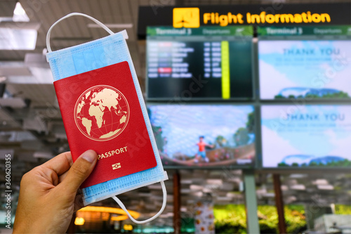 Canvas Print Traveller holding passport and face mask in airport, in front of Flight information board